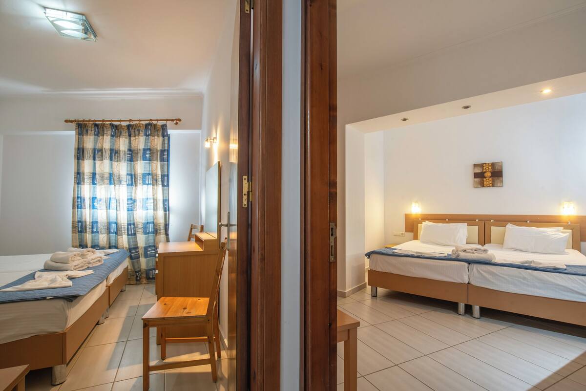 A hotel room with two beds, a wooden desk, a chair, and a window with curtains.