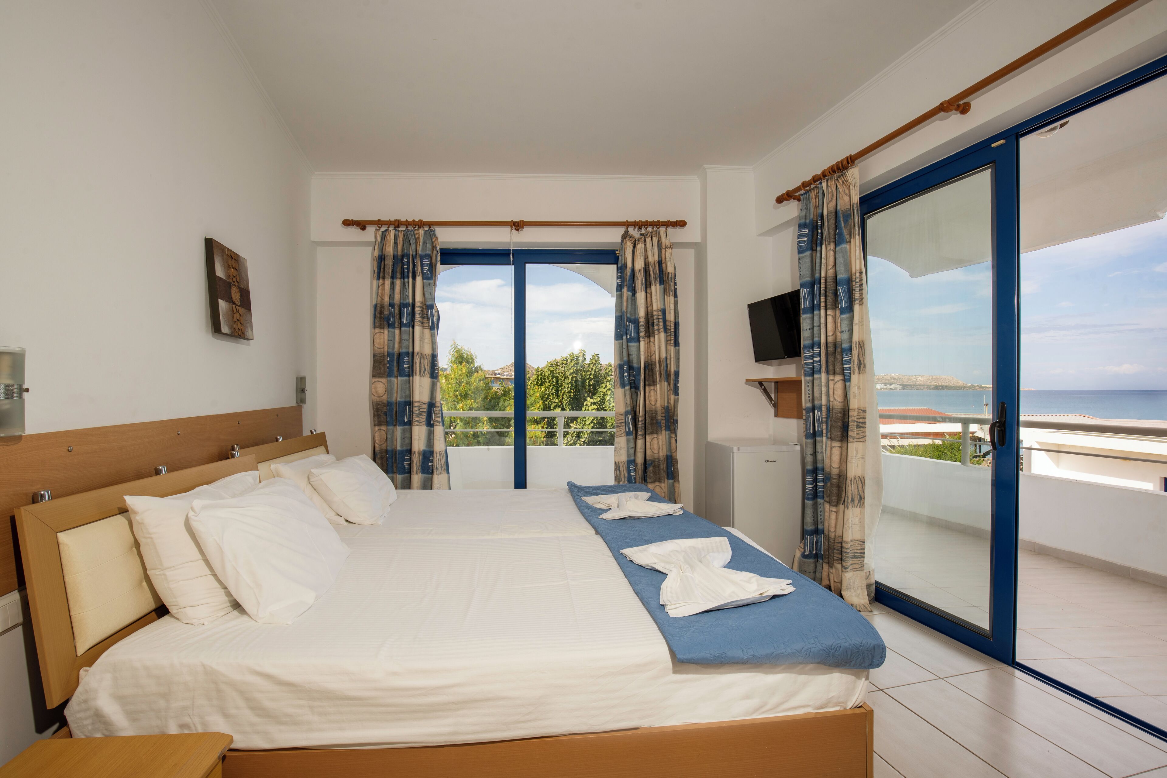 Quarto de hotel com uma cama grande, televisão e varanda com vista para o mar.