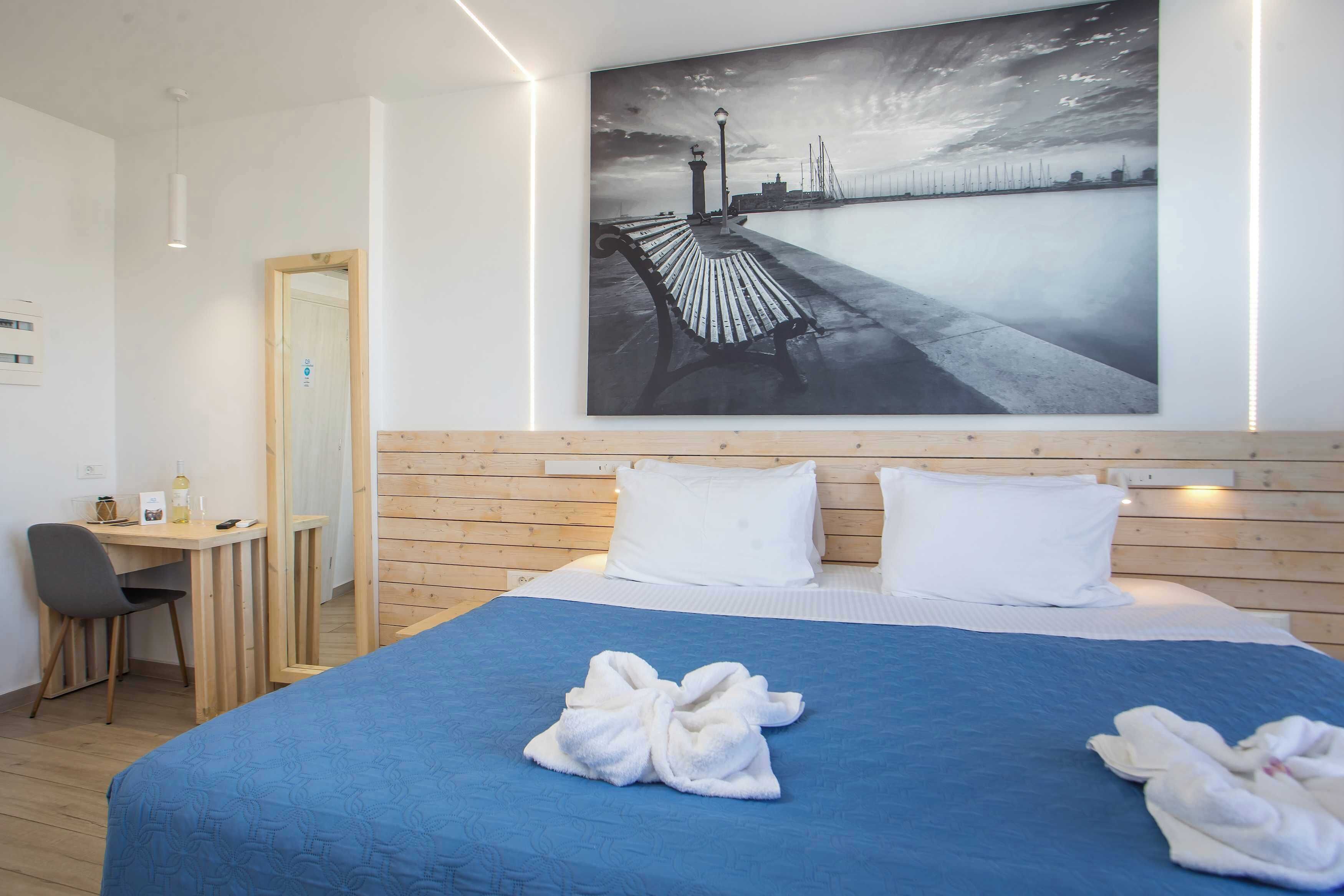 A hotel room with a bed, a desk, a chair, and a large wall painting.