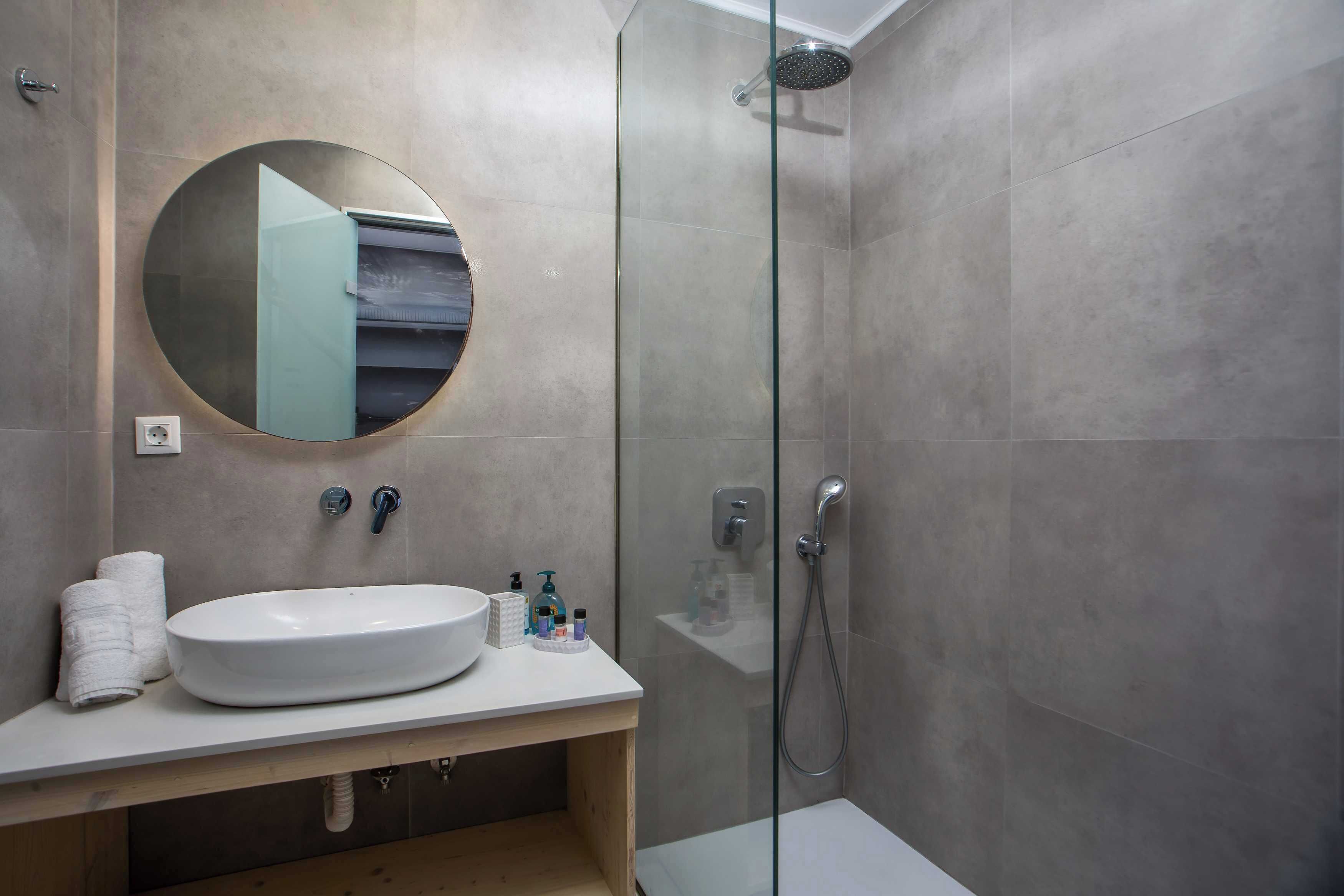 A modern bathroom with a round mirror, a sink, a glass-enclosed shower, and a wooden vanity.