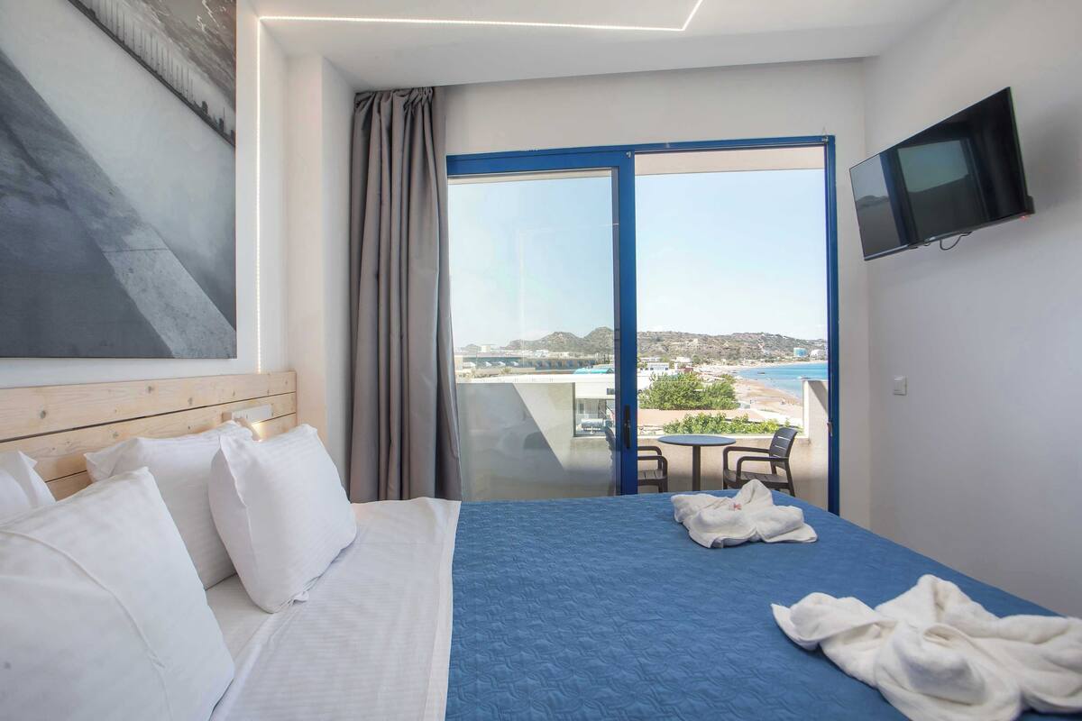 A hotel room with a bed, a TV, a balcony with a view, and a table with chairs.