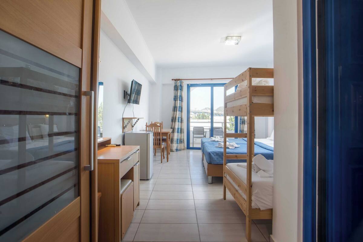 A room with a bunk bed, a desk with a chair, a television, and a window with curtains.