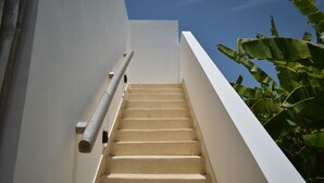 Eine Treppe mit Handlauf, die nach oben führt, umgeben von weißen Wänden und blauem Himmel.