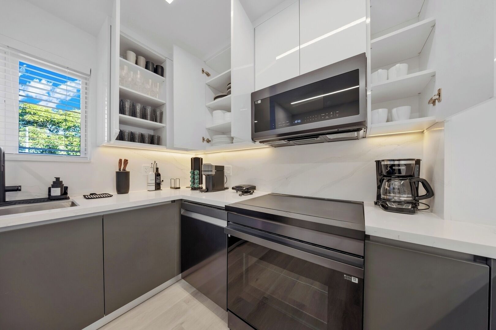 Une cuisine moderne dotée d’appareils électroménagers intégrés, de meubles blancs et d’une fenêtre donnant sur un espace verdoyant.