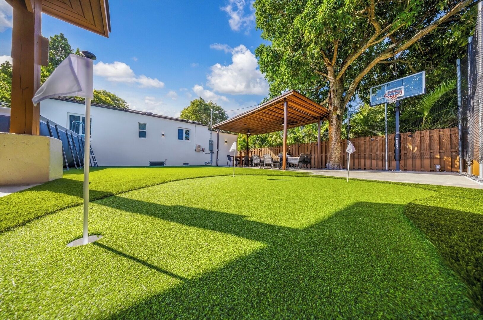 A backyard with artificial grass, a basketball hoop, and a covered seating area.