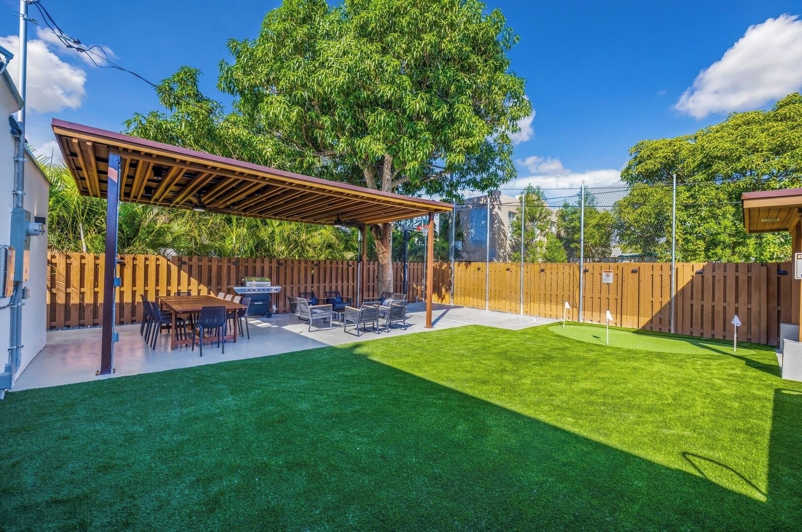 A backyard with a wooden pergola, a barbecue grill, and a dining table with chairs.