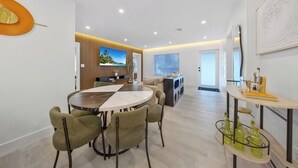 A modern living room with a round dining table, green upholstered chairs, a flat-screen TV, a kitchen area, and a glass display case with bottles. - New Design Dist Gem:Pool,HotTub,Minigolf,Nespresso (Miami)