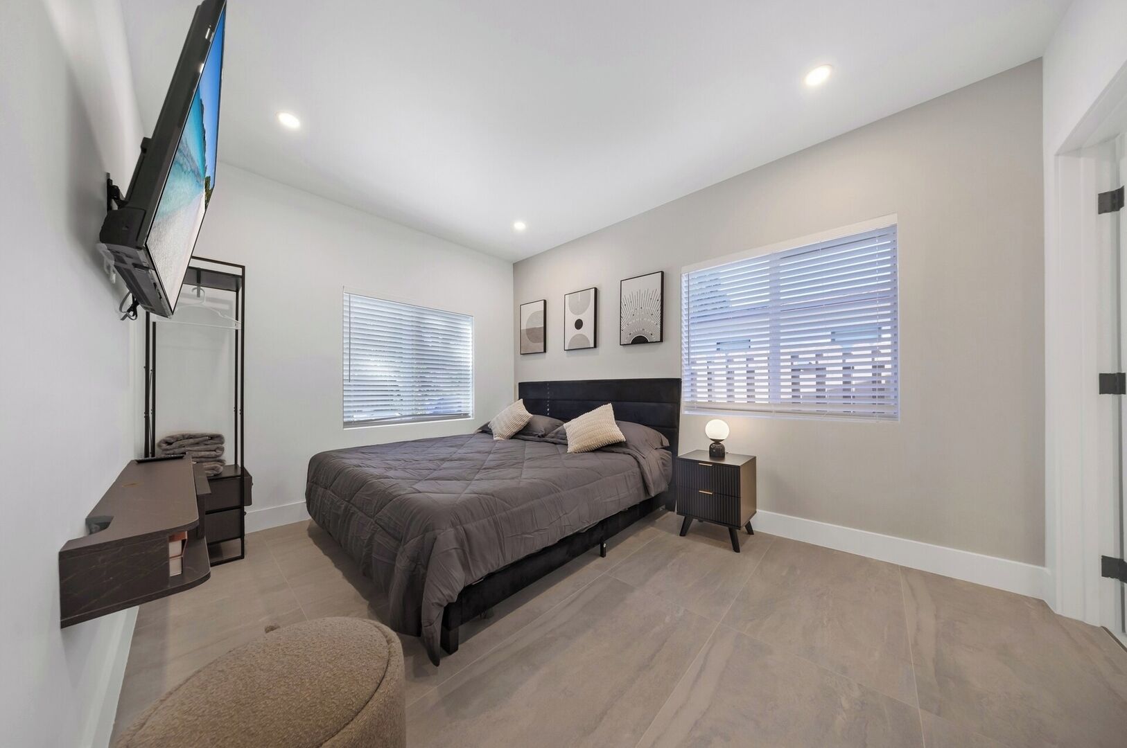 A modern bedroom with a bed, bedside tables, a TV, and large windows.