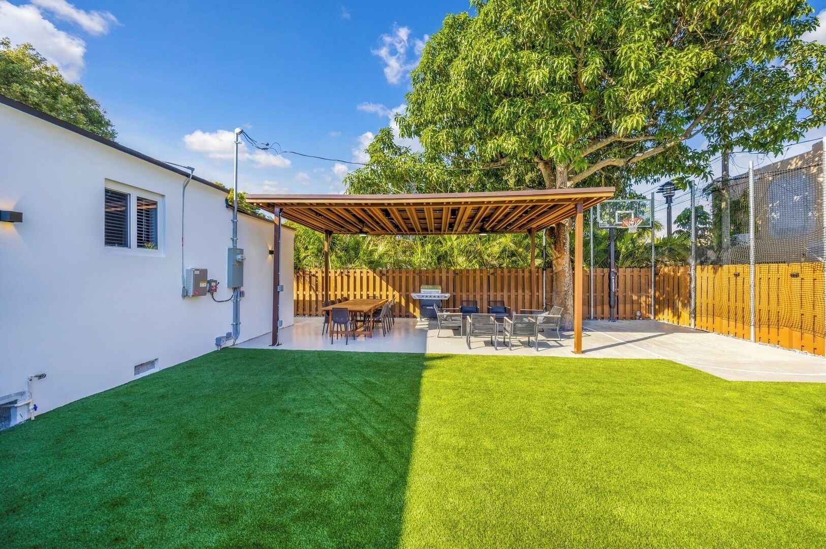 A backyard with a wooden pergola, a barbecue area, and a fenced basketball court.