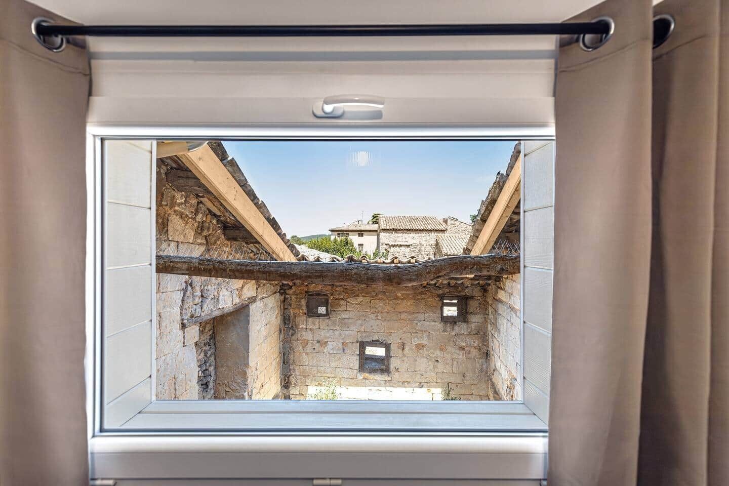 Una ventana que ofrece vista a un antiguo edificio de piedra con tejado de tejas.
