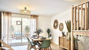 A dining area with a wooden table, green chairs, and a glass door leading to an outdoor patio. - Cozy duplex - patio - sleeps 6 - historic village (Saint-Paul-Trois-Châteaux)