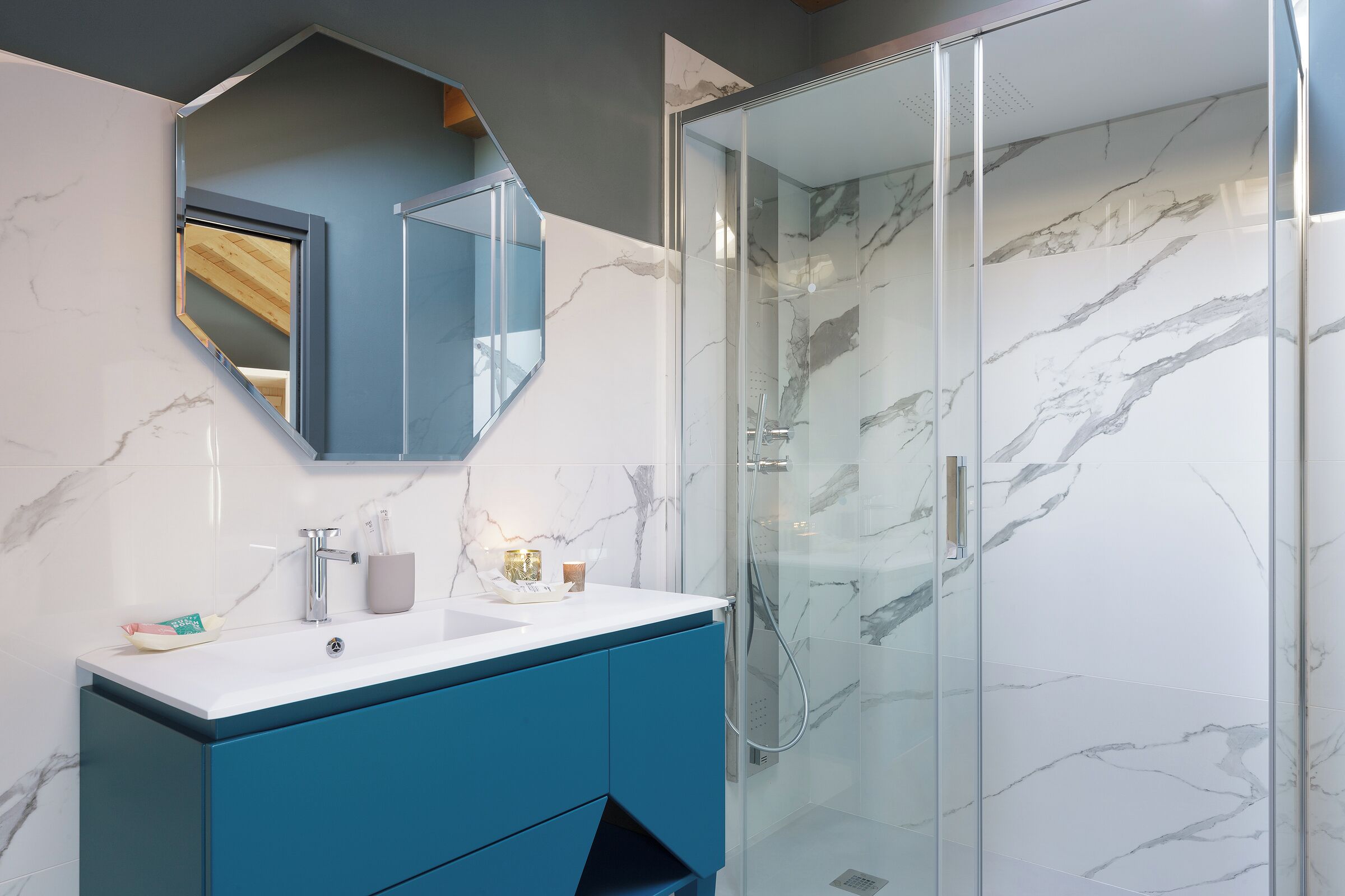 A modern bathroom with a marble shower, a sink with a blue cabinet, and a large mirror.