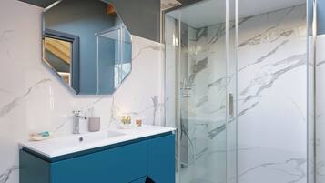 A modern bathroom with a marble shower, a sink with a blue cabinet, and a large mirror.