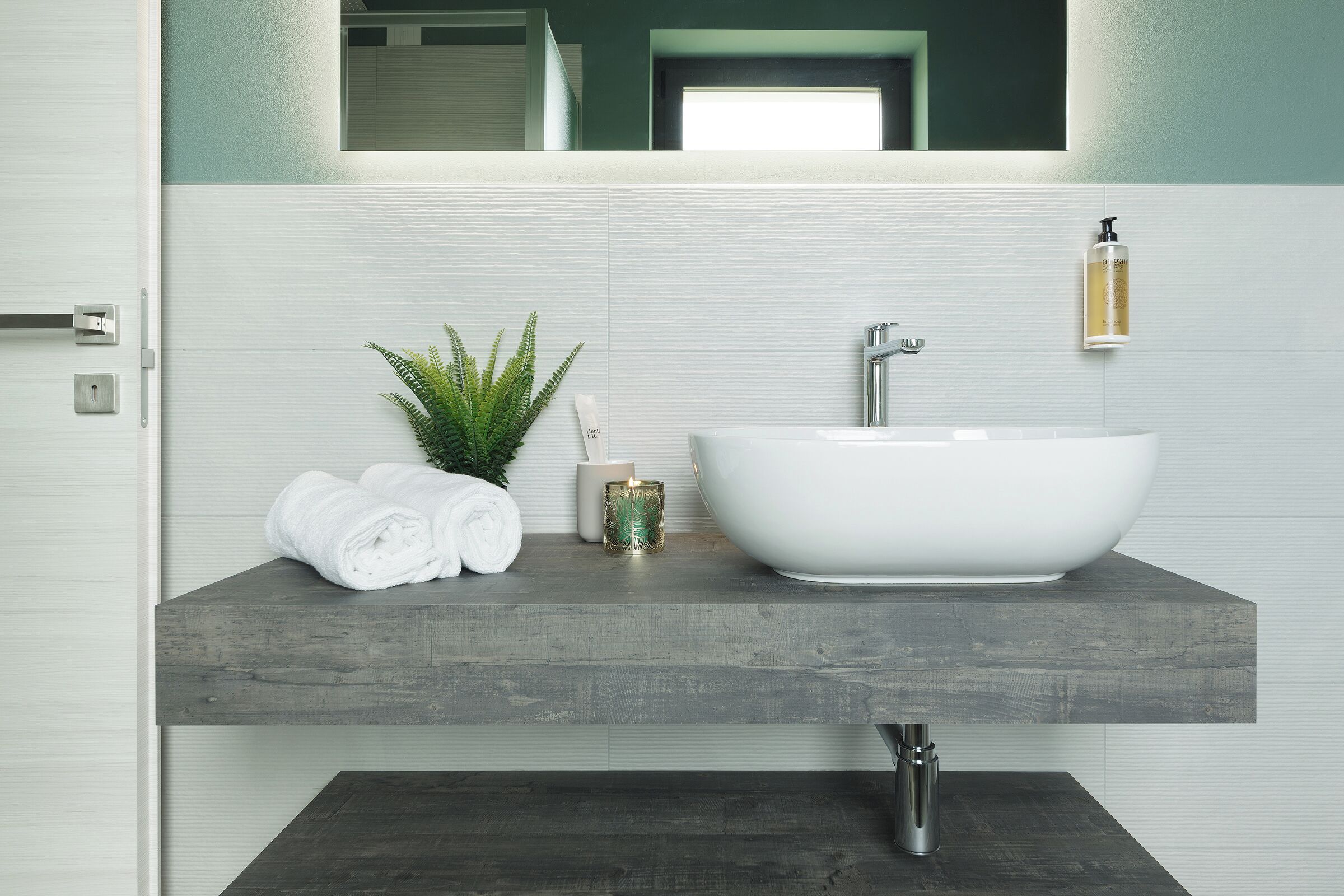 A bathroom with a white sink, a towel rack, a small plant, and a candle.