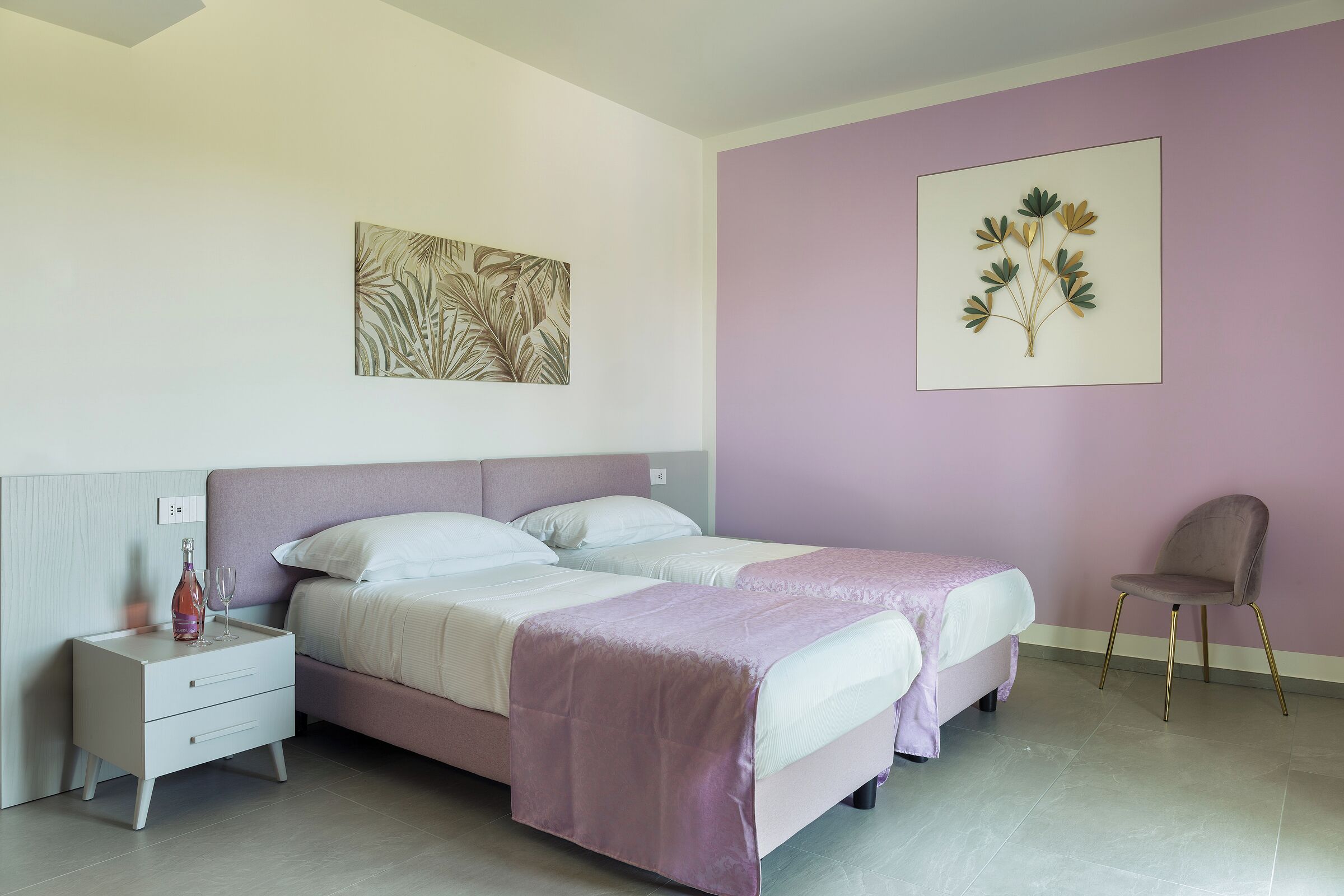 A bedroom with two beds, a nightstand, a chair, and artwork on the walls.