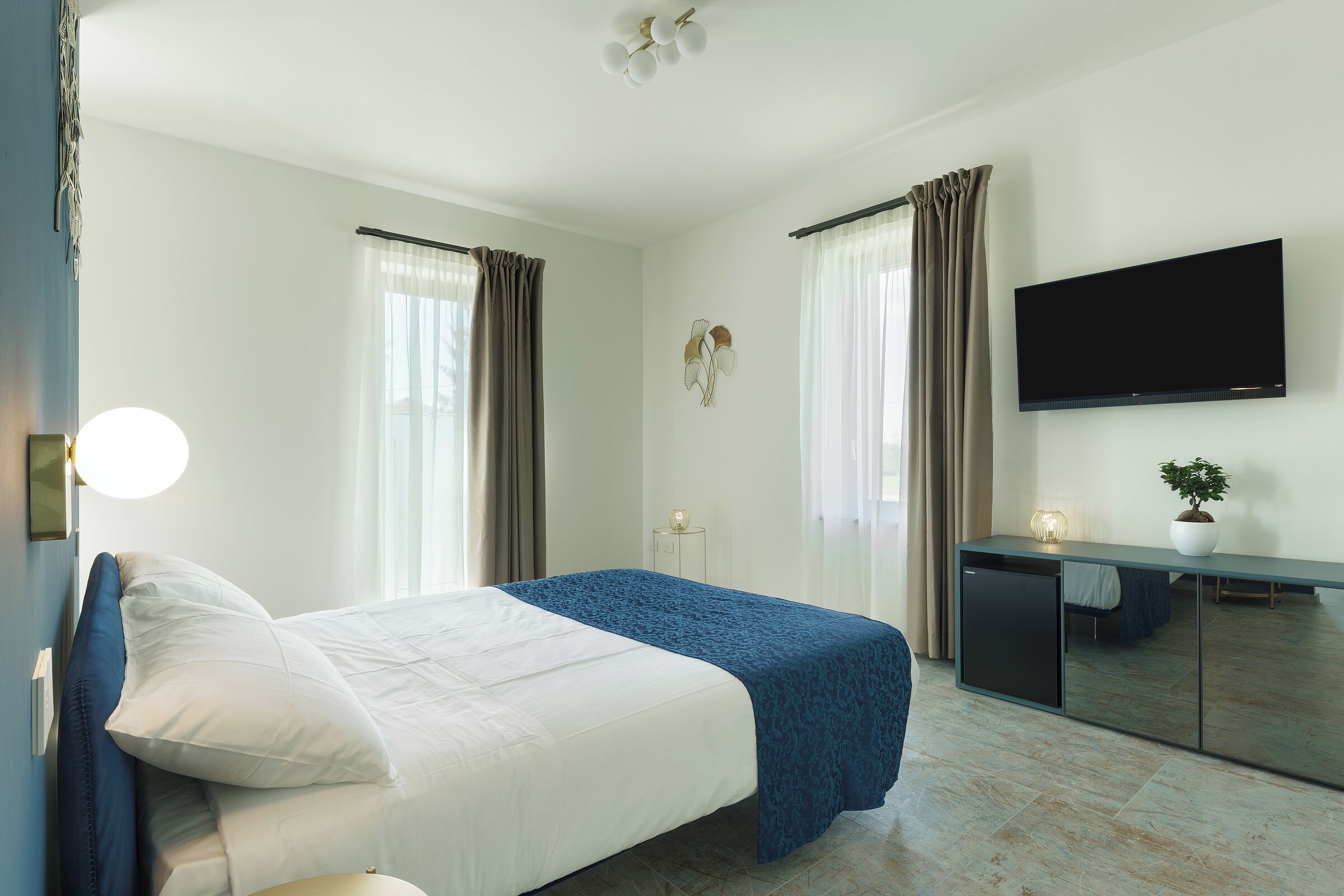 Une chambre d’hôtel avec un lit, un bureau, une télévision et une plante en pot.