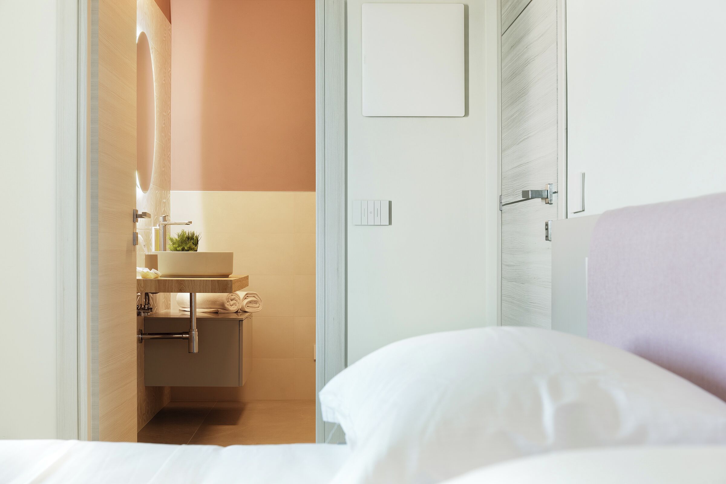 A hotel room with a bed, a bathroom with a sink, and a door.