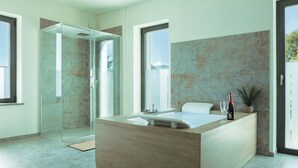 Un baño moderno con cabina de ducha de vidrio, una bañera grande y una zona de lavabo con una botella de vino y copas.