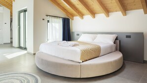 Un dormitorio moderno con una cama curvada, vigas de madera en el techo y vistas al exterior.