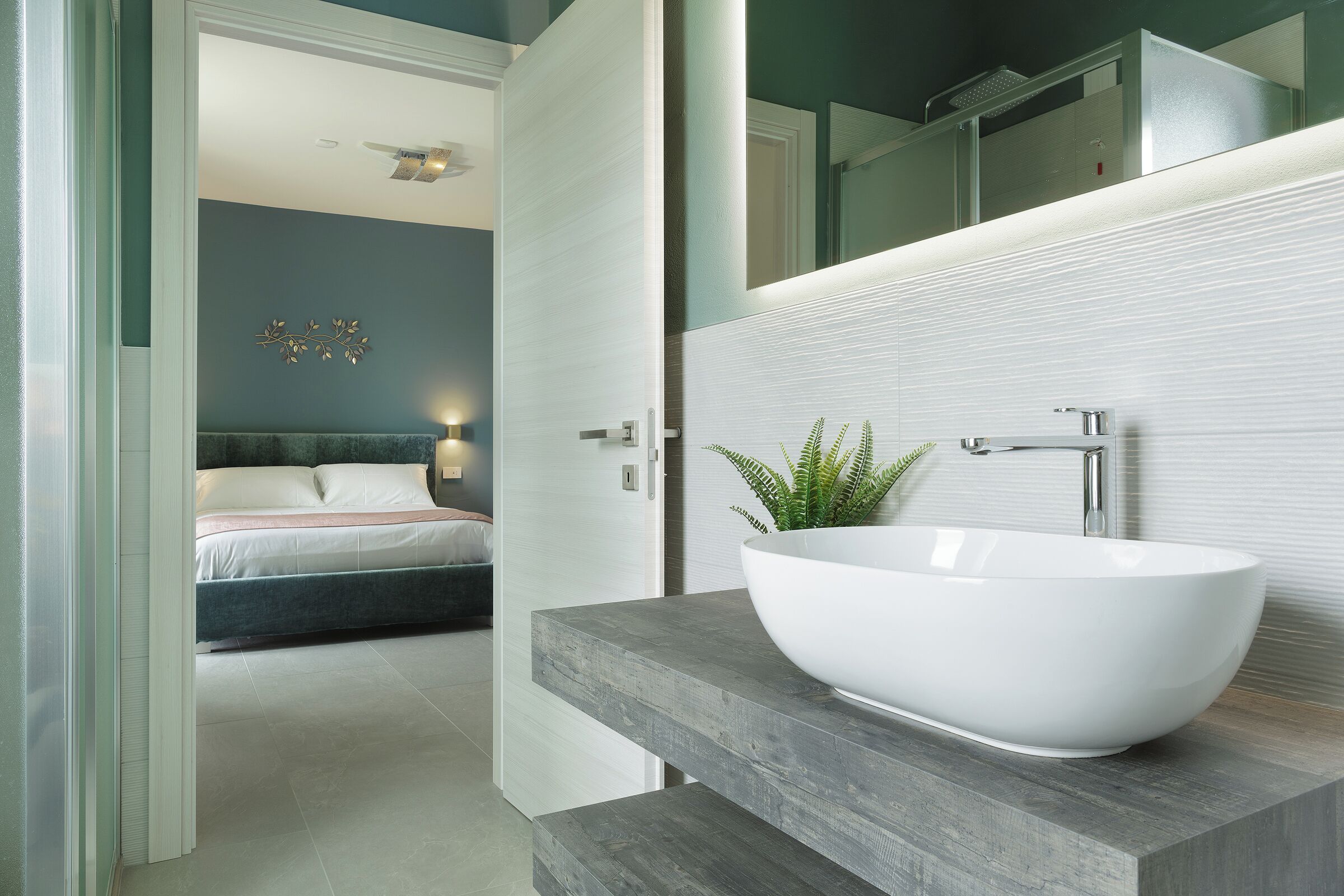 A modern bathroom with a large white vessel sink, a mirror, and a potted plant.