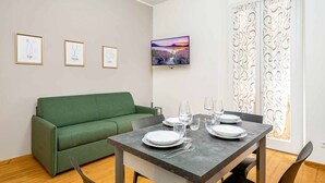 Un coin repas avec une table dressée pour quatre personnes, un canapé vert et des œuvres d’art encadrées accrochées aux murs.
