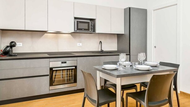 Une cuisine moderne avec des meubles gris, un micro-ondes encastré, un four et une table à manger dressée avec des assiettes et des verres.