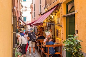 Une rue étroite avec des tables en terrasse, une enseigne de boulangerie et une porte verte.