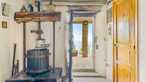 Un intérieur rustique avec un pressoir en bois, un chemin de pierre menant à l’extérieur et une porte en bois.