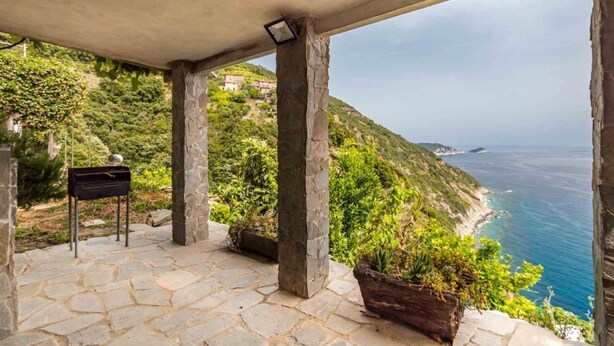 Un espace extérieur pavé de pierres, offrant une vue sur la mer et les collines.