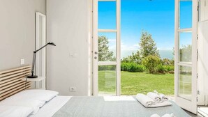 A bedroom with a bed, a bedside lamp, and a view of a garden through open doors. - Sea Forest - Ginko, Sea Lands (Bonassola)