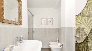 A modern bathroom with a large white sink, a mirror with a floral frame, a bidet, and two framed pictures on the wall. - Sea Forest - Ginko, Sea Lands (Bonassola)