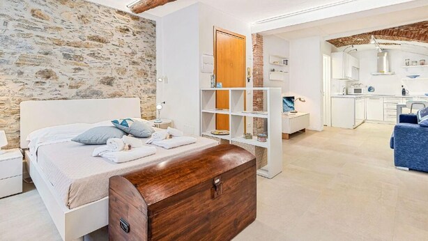 A bedroom with a stone wall, a wooden chest, a bed with pillows, a white wardrobe, and a blue sofa. - Tin Box, TerreMarine (Riomaggiore)