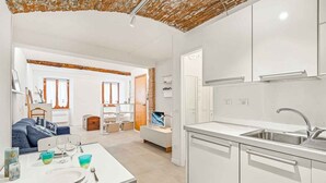 A modern kitchen with white cabinets, a stainless steel sink, and a dining area with a table set for two. - Tin Box, TerreMarine (Riomaggiore)