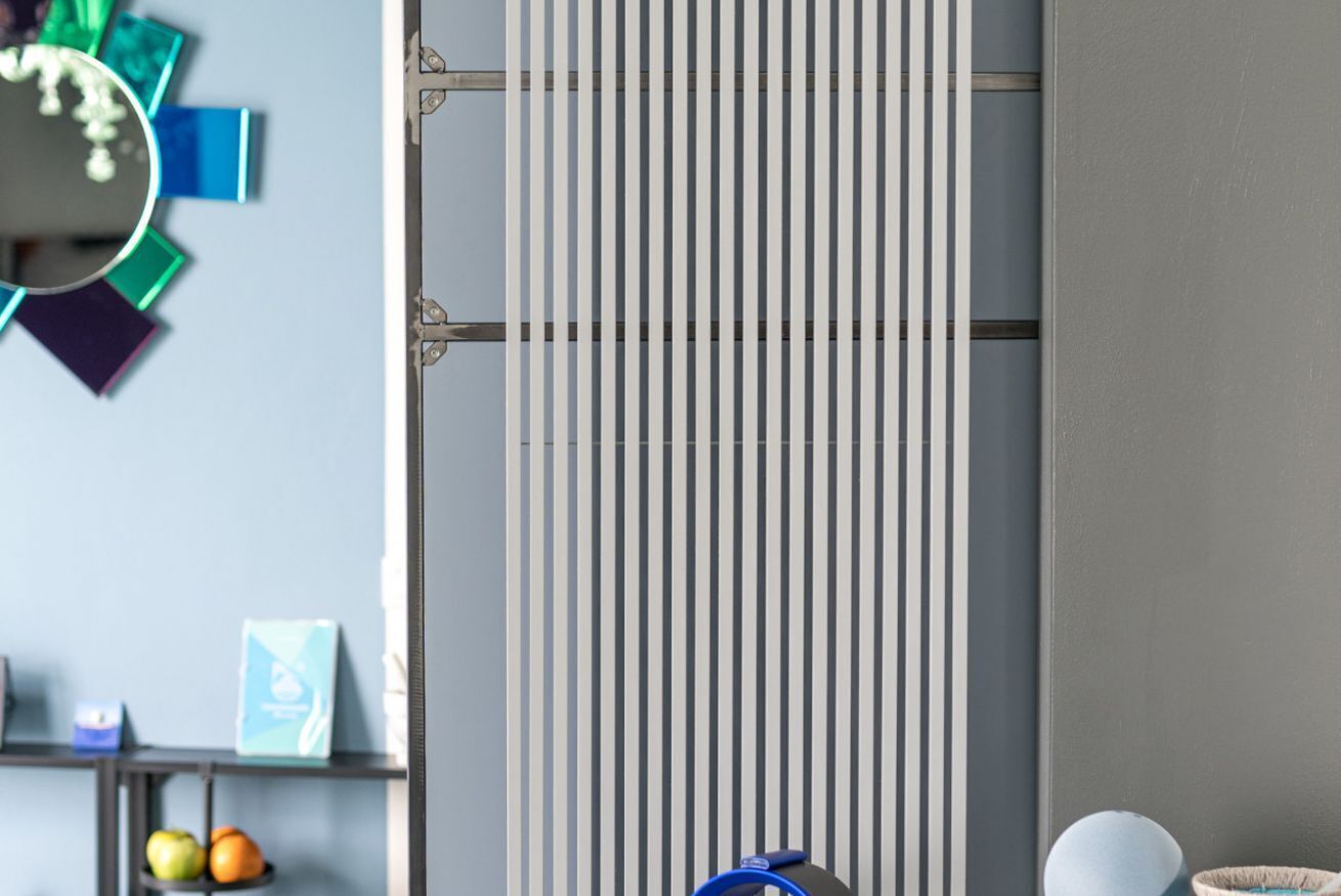 A modern room with a vertical blinds panel, a shelf with fruits, and a blue object on the floor.