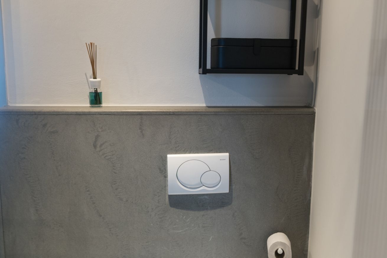 Une salle de bain avec un mur gris à texture, des toilettes blanches et un meuble à pharmacie noir.