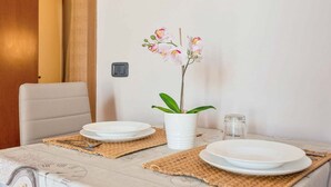 Une table à manger avec deux assiettes blanches, un vase blanc contenant une plante et un bocal en verre.