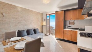Une cuisine moderne avec des meubles en bois, un coin repas avec une table dressée pour deux personnes, et un balcon avec vue.
