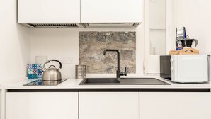 Een moderne keuken met witte kastjes, een roestvrijstalen waterkoker, een koffiezetapparaat en een magnetron.