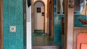 A hallway with green tiled walls, a wooden staircase, and a view into another room.