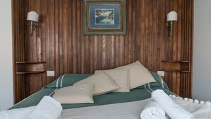 A neatly made bed with green and beige bedding, two wall-mounted lamps, and a framed picture on the wooden wall.