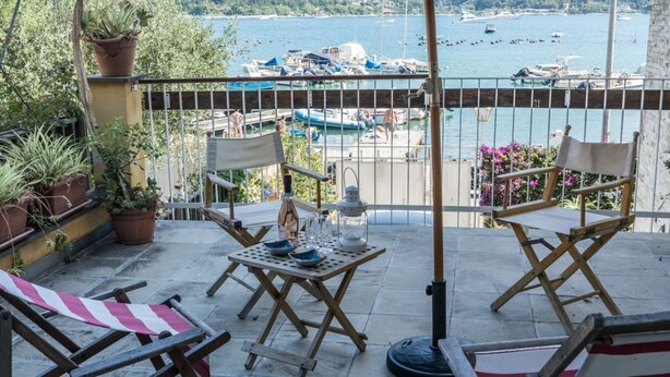 A balcony with a table, chairs, potted plants, and a view of boats on the water.