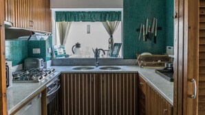 A compact kitchen with two sinks, wooden cabinets, a gas stove, and a window with curtains.