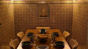 Een eethoek met een lange houten tafel gedekt voor een maaltijd, omringd door muren met een patroon en een gedetailleerd plafond.