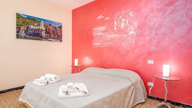 A hotel room with a bed, two bedside tables, a painting on the wall, and a red accent wall. - Ca dei Tiè, TerreMarine (Riomaggiore)