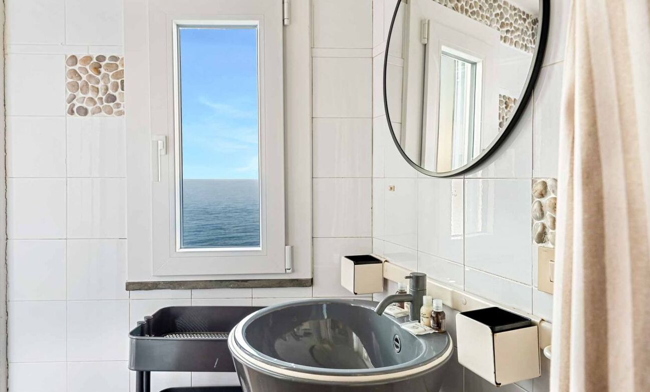 Ein Badezimmer mit einem großen Fenster, einem runden Spiegel und einer Badewanne.