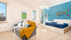Een moderne hotelkamer met een bank, een bed, een blauwe accentmuur, een wenteltrap en een welkomstposter.