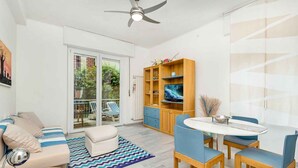 A modern living room with a sofa, a dining table with chairs, a television, and a ceiling fan. - Corner 89, TerreMarine (Monterosso al Mare)