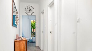 A hallway with a wooden side table, a clock, and a door leading to a room with a blue door. - Corner 89, TerreMarine (Monterosso al Mare)