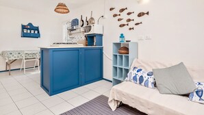 Un espace de vie compact comprenant un coin cuisine, un coin repas et un canapé agrémenté de coussins à motifs.