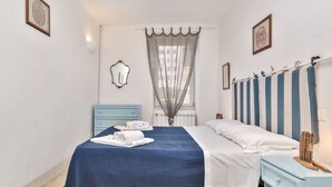 Une chambre à coucher comprenant un lit, une table de chevet, une commode, une fenêtre avec des rideaux légers et des œuvres d’art accrochées au mur.